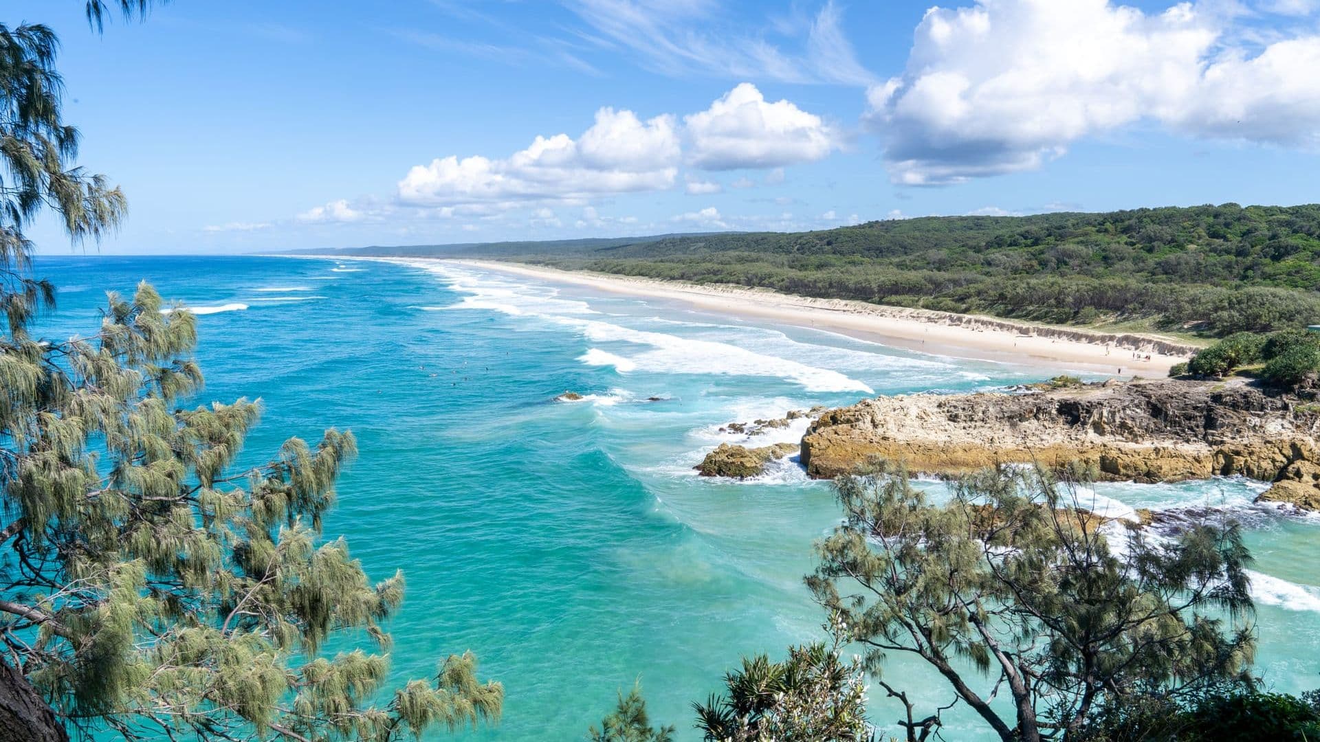 Elevated view down a long sandy beach with turquoise waves and a rocky foreshore on North Stradbroke Island