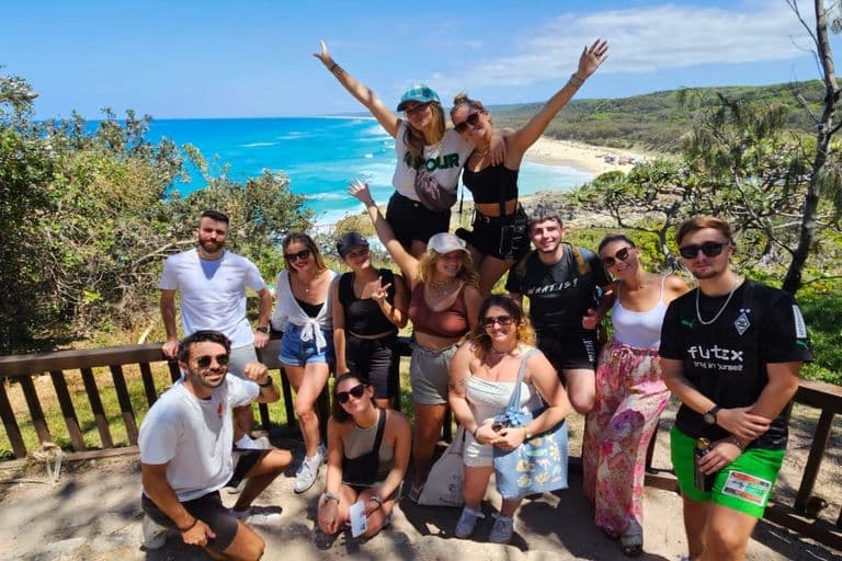Tour group posing at Backpackers Lookout above a long sandy beach on North Stradbroke Island