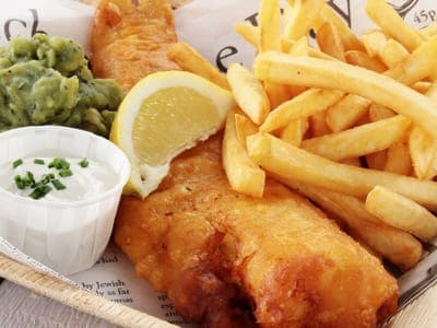 A basket of golden beer-battered fish and chips with mushy peas, lemon and tartare