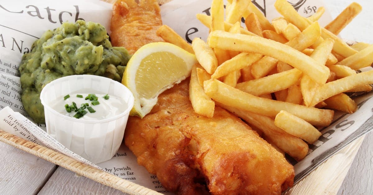 A basket of golden beer-battered fish and chips with mushy peas, lemon and tartare
