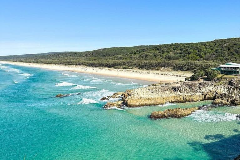 Coastal vista of turquoise water, rocky headland and long sandy beach on Minjerribah (North Stradbroke Island)