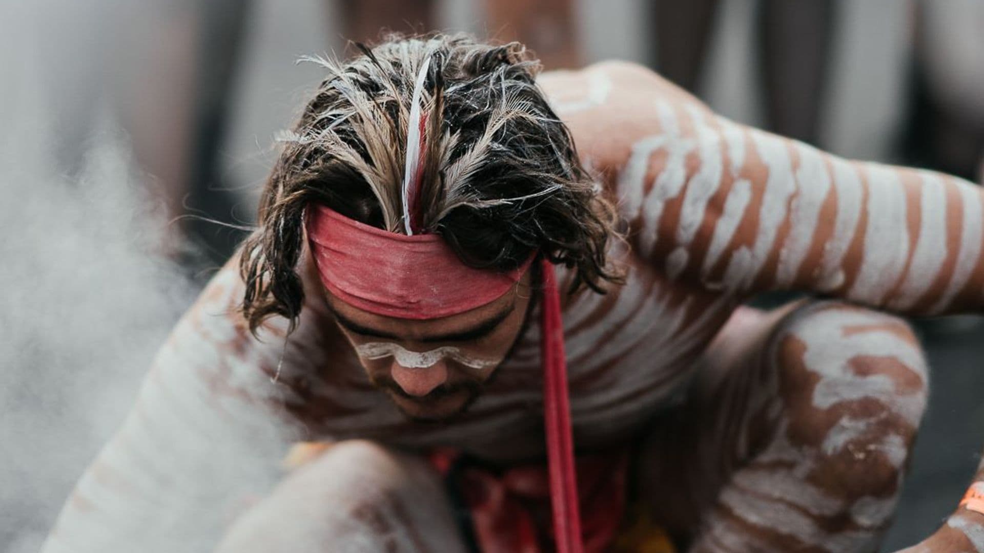 An Aboriginal man participates in a smoking ceremony, surrounded by cleansing smoke, with hands covering her face in a moment of reflection. A sacred ritual in Indigenous Australian culture, often performed to welcome visitors and protect Country.