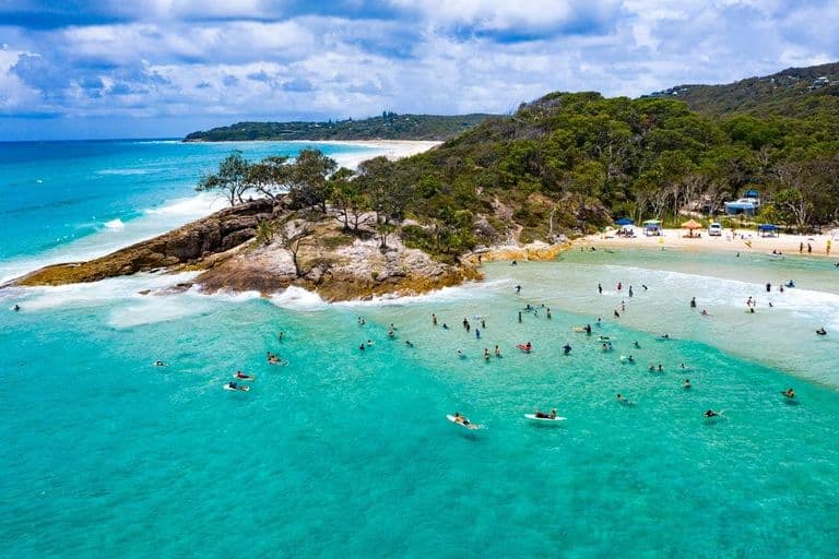 Aerial view of swimmers and paddlers in the turquoise water at Cylinder Beach, North Stradbroke Island