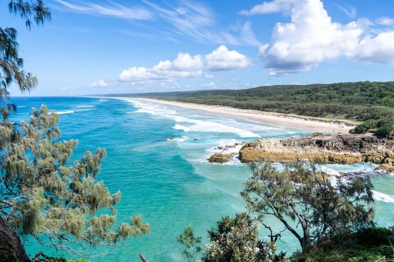 Elevated view down a long sandy beach with turquoise waves and a rocky foreshore on North Stradbroke Island