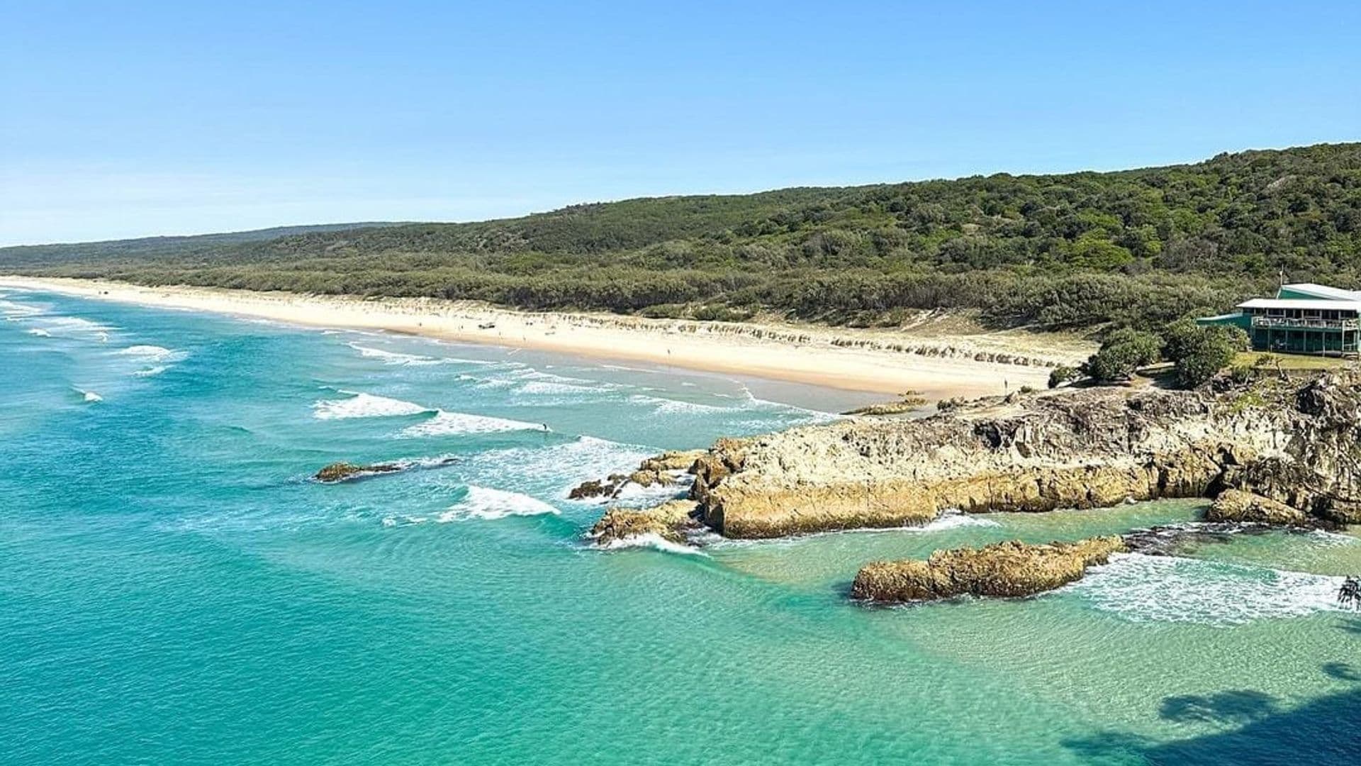 Coastal vista of turquoise water, rocky headland and long sandy beach on Minjerribah (North Stradbroke Island)